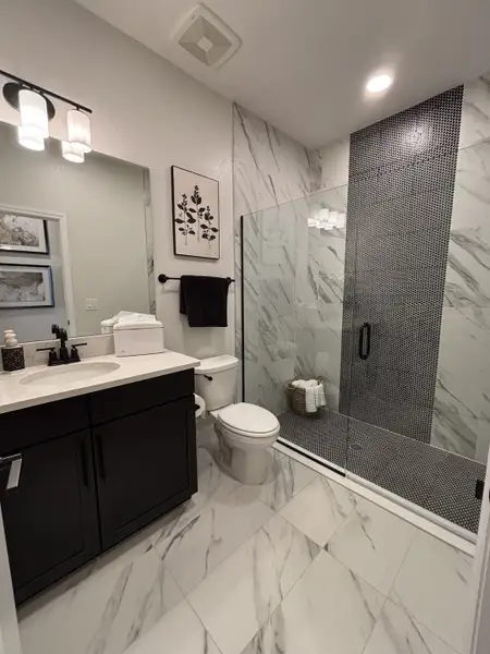 A stylish bathroom featuring a blue accent wall, a classic white vanity, and a tiled bathtub in Eden at Crossprairie by M/I Homes (St. Cloud, FL).