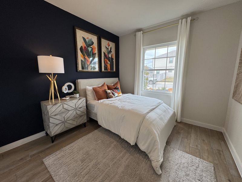 A cozy bedroom with a navy accent wall, framed art, and modern decor, featuring a plush bed and elegant bedside lighting.