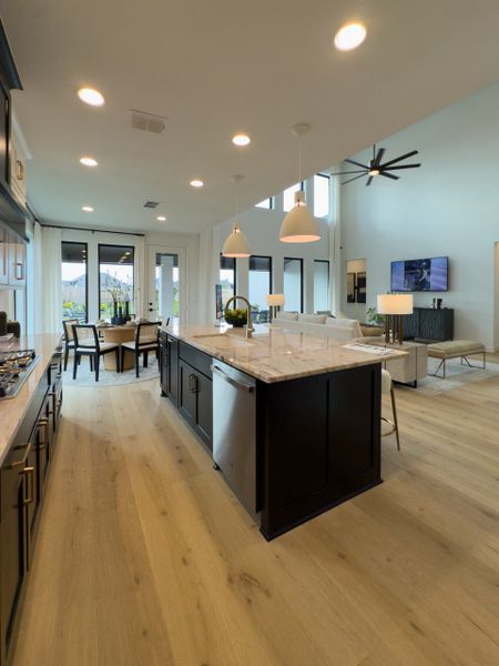 A modern kitchen with light wood floors, a large island, pendant lighting, and an open dining-living area. A modern kitchen with light wood floors, a large island, pendant lighting, and an open dining-living area.