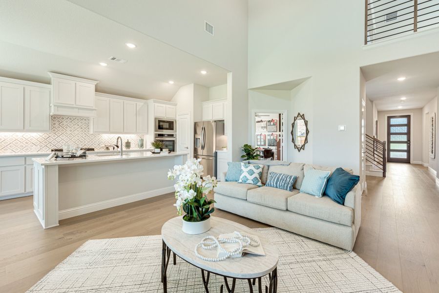 Open-concept living room and kitchen with high ceilings, white cabinets, hardwood floors, and a beige sofa with blue pillows Open-concept living room and kitchen with high ceilings, white cabinets, hardwood floors, and a beige sofa with blue pillows