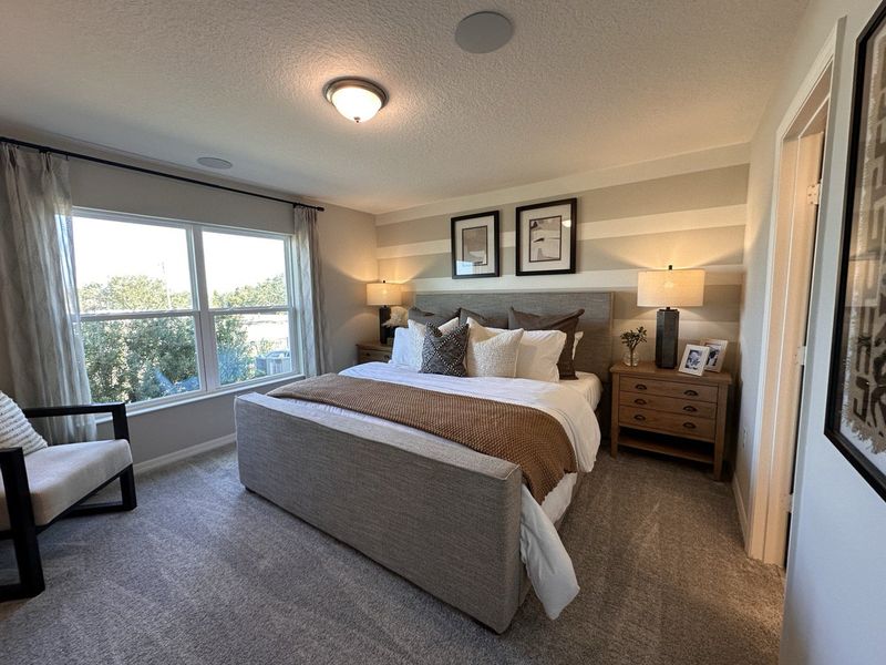 A cozy bedroom with a neutral color scheme, modern lighting, and striped accent walls in Landings at Lake Mabel Loop by KB Home (Dundee, FL).