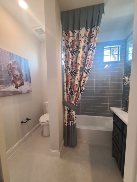 A cozy bathroom featuring floral drapery, light tiles, and soft lighting, with a charming dog portrait decorating the wall. A cozy bathroom featuring floral drapery, light tiles, and soft lighting, with a charming dog portrait decorating the wall.
