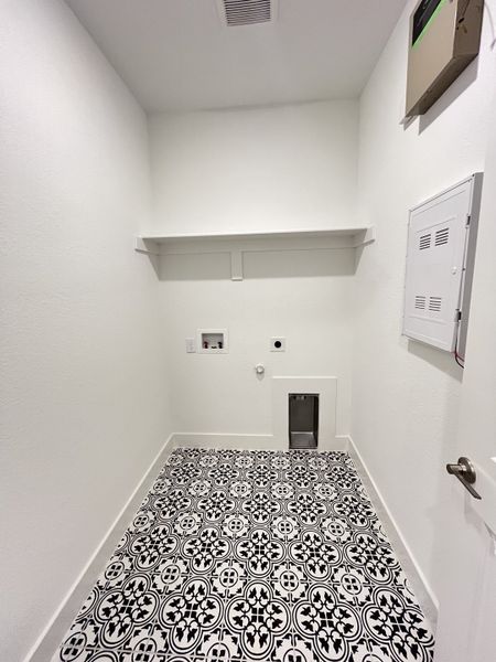 A utility room with striking black-and-white patterned tiles, a wall shelf, and laundry hookups. A utility room with striking black-and-white patterned tiles, a wall shelf, and laundry hookups.
