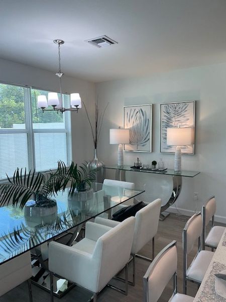 A chic dining room with a glass table, white chairs, modern lighting, and decorative art, creating an elegant atmosphere.