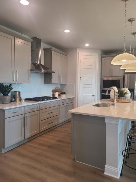 A modern kitchen with sleek gray cabinets, stainless steel appliances, and elegant pendant lighting over a spacious island.