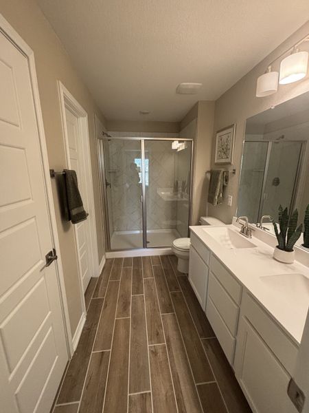 A modern bathroom with wood-look tile flooring, a glass shower, dual sinks, and stylish lighting. A modern bathroom with wood-look tile flooring, a glass shower, dual sinks, and stylish lighting.