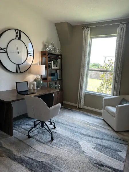 A modern home office with a sleek desk, cozy chair, and large decorative wall clock by the window.