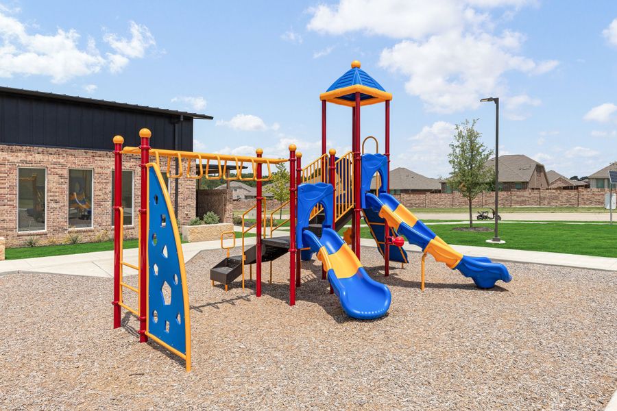 Community playground with blue and yellow slides, climbing wall, and monkey bars on wood chip surface