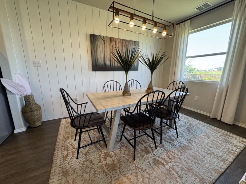 A chic dining room with a rustic table, elegant chairs, and a large window. Features a modern light fixture and nature artwork.
