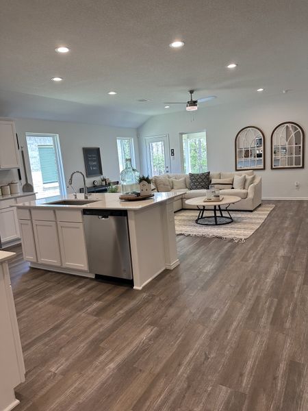 An open-concept living space with wood flooring, modern kitchen, and cozy seating area, brightened by natural light.