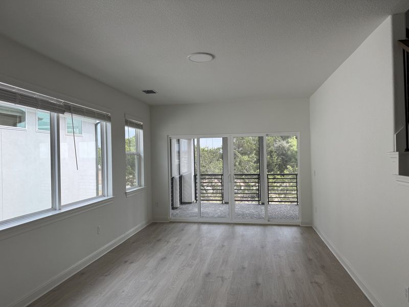 Bright room with sleek wood floors, ample windows, and a balcony overlooking greenery. Perfect for modern, serene living.