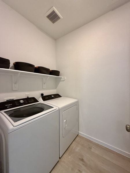 A functional laundry room featuring a modern washer, dryer, and open shelving for storage baskets. A functional laundry room featuring a modern washer, dryer, and open shelving for storage baskets.