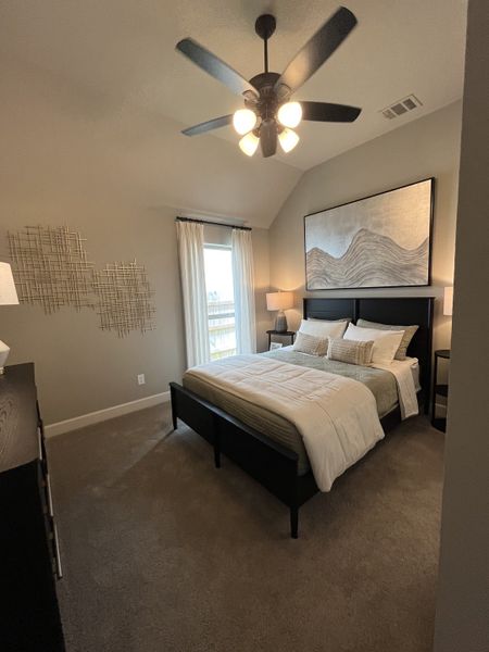 A cozy bedroom with a plush carpet, chic art, and a modern ceiling fan, creating a serene retreat.