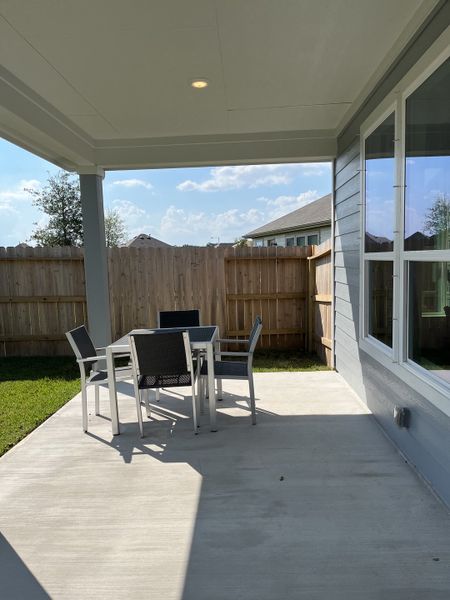 A modern patio with sleek outdoor furniture and a fenced yard, perfect for relaxing under a spacious covered area.