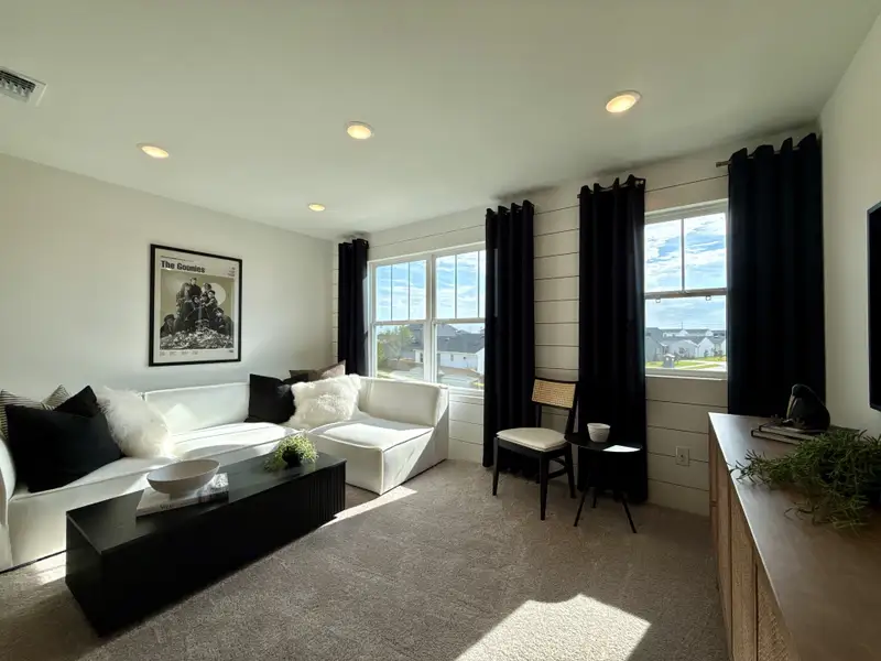 A cozy living room with a white sectional sofa, dark drapes, and movie poster art, bathed in natural light. A cozy living room with a white sectional sofa, dark drapes, and movie poster art, bathed in natural light.