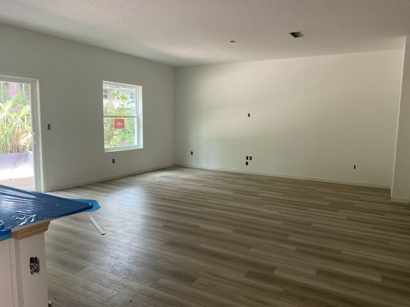 An open living space with light wood flooring, white walls, and large windows allowing natural light to filter through.