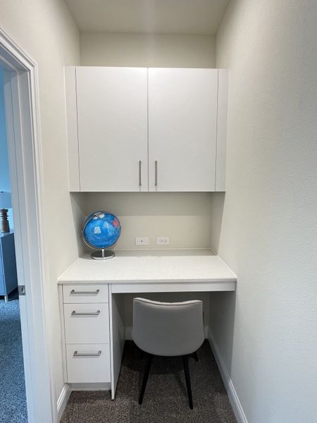 A compact study nook with white cabinetry, a sleek chair, and a tidy desk, offering a cozy workspace.