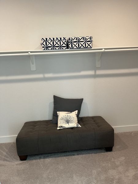A cozy carpeted space with a gray bench, decorative pillows, and patterned storage boxes on a shelf.