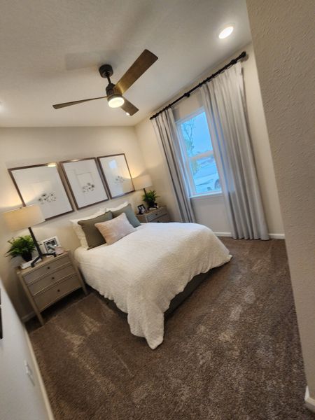A cozy bedroom featuring a ceiling fan, elegant artwork, neutral décor, and plush carpeting. A cozy bedroom featuring a ceiling fan, elegant artwork, neutral décor, and plush carpeting.