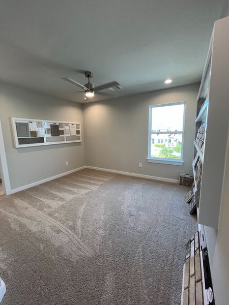 A cozy room with plush carpeting, neutral walls, ceiling fan, and ample natural light from a large window. A cozy room with plush carpeting, neutral walls, ceiling fan, and ample natural light from a large window.