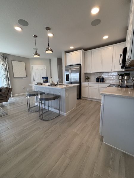 A sleek, modern kitchen with white cabinetry, stainless steel appliances, and pendant lighting in Eden at Crossprairie by M/I Homes (St. Cloud, FL).