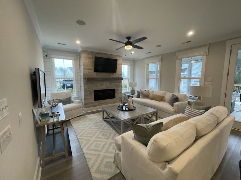 A cozy living room featuring a fireplace with a wood accent wall, plush white sofas, and large windows offering plenty of natural light.