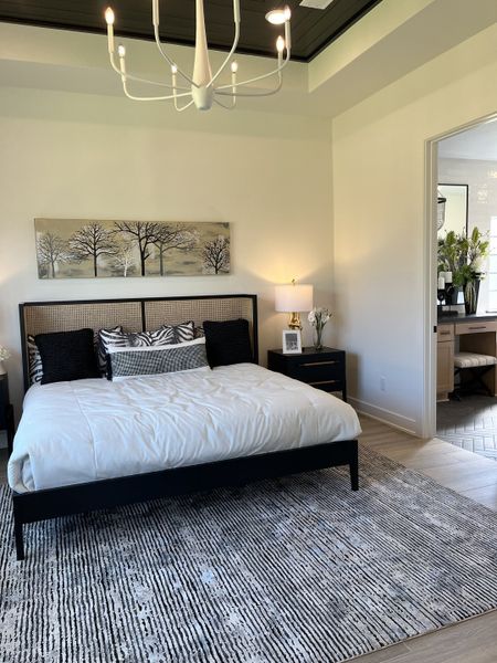 A serene bedroom featuring a chic chandelier, modern artwork, and a cozy bed on a textured rug.