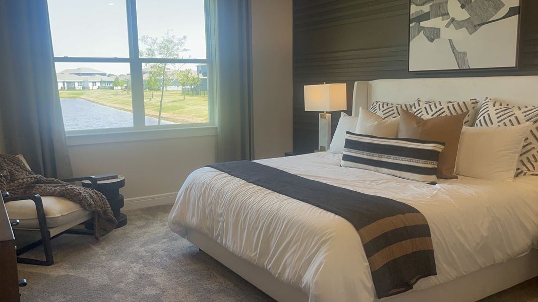A cozy bedroom with a plush bed, modern decor, and a large window offering a serene water view.