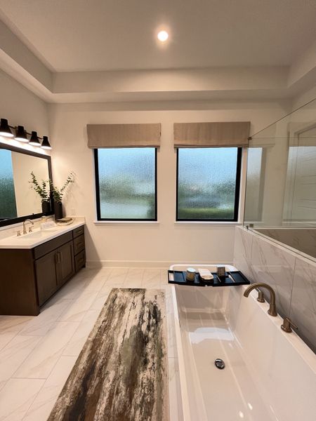 A contemporary bathroom featuring a sleek bathtub, double vanity, and large windows for natural light.