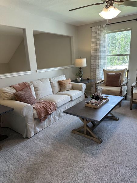 A cozy living room featuring a plush white sofa, elegant armchair, and rustic coffee table beneath a ceiling fan.