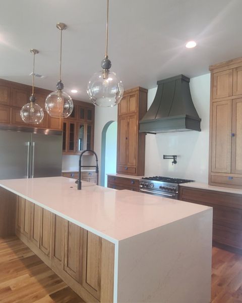 A modern kitchen with wooden cabinetry, sleek countertops, and elegant pendant lighting.