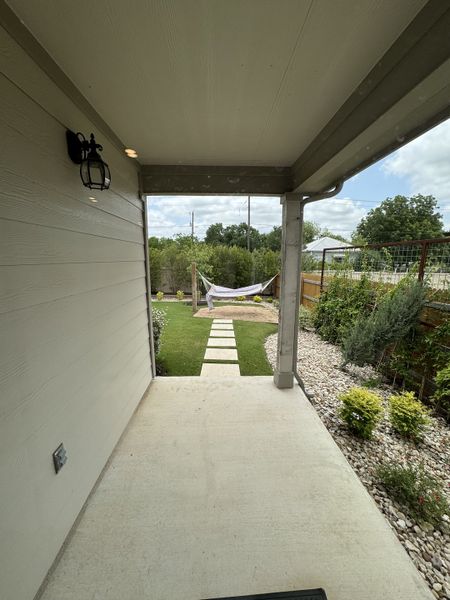 A cozy covered patio with a walkway leading to a hammock and a lush garden view.