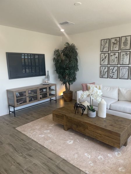 A cozy living room with a white sofa, wooden coffee table, and botanical wall art, complemented by warm wood flooring.