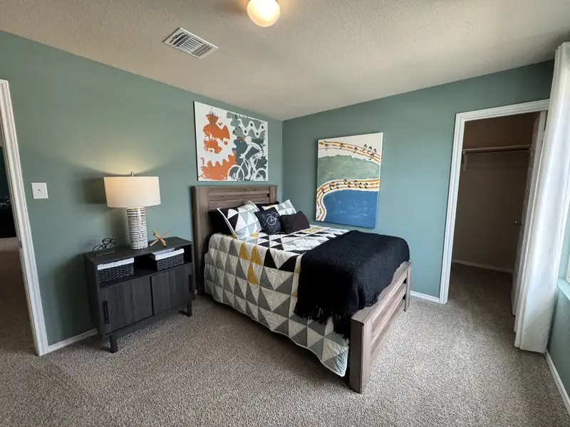 A cozy bedroom featuring a modern bed, geometric quilt, and artistic wall decor, complemented by soft carpeting and subtle lighting.