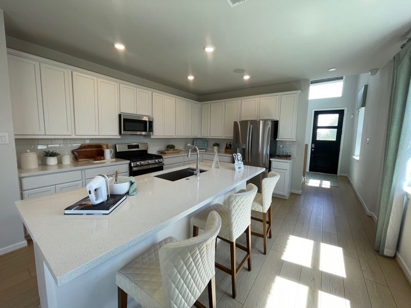 A modern kitchen featuring white cabinetry, a large island with seating, and stainless steel appliances.