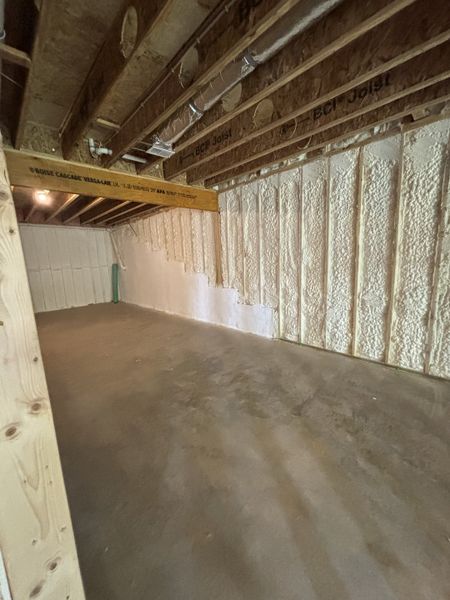 A spacious unfinished basement with spray foam insulation and exposed wooden beams, perfect for customization.