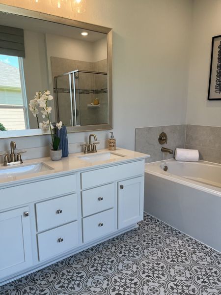 A chic bathroom featuring a dual-sink vanity, ornate patterned flooring, and a cozy built-in bathtub.