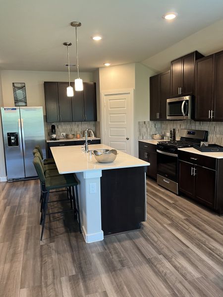 A modern kitchen with dark cabinets, a large island, stainless steel appliances, and elegant pendant lighting.