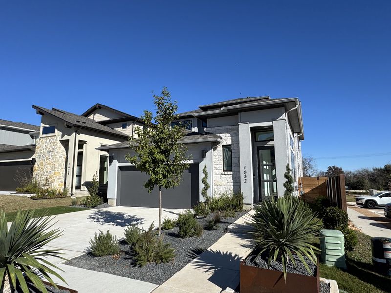 A sleek modern home with clean lines, stone accents, and lush landscaping in Old Town East by Perry Homes (Pflugerville, TX).