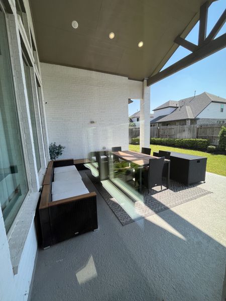 A cozy outdoor patio with wicker seating and a dining table under a modern, covered roof, perfect for relaxation.