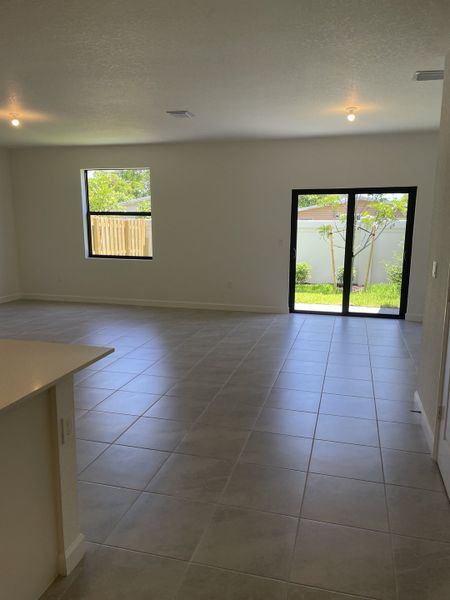 Spacious living area with large windows, tile flooring, and sliding glass doors opening to a green yard.