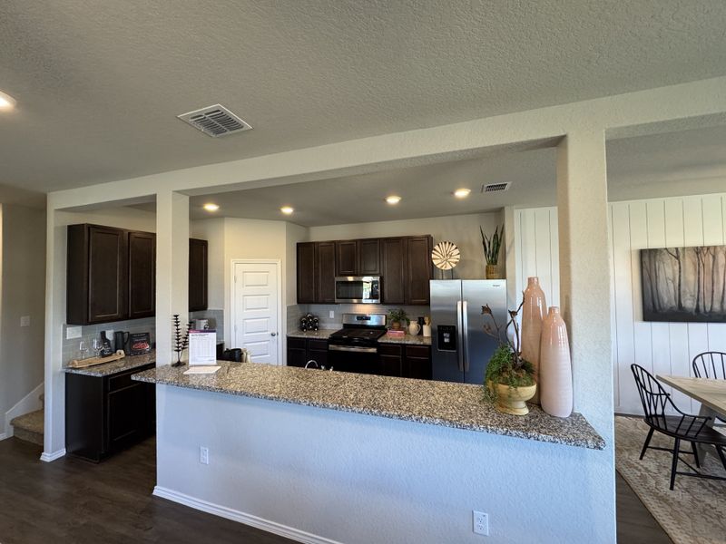 A modern kitchen with dark wood cabinets, granite countertops, and stainless steel appliances, opening to a dining area.