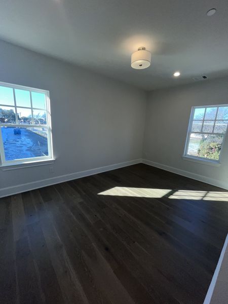 A bright room with dark hardwood floors, two windows providing ample natural light, and a modern ceiling light fixture. A bright room with dark hardwood floors, two windows providing ample natural light, and a modern ceiling light fixture.