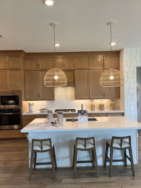 A modern kitchen with wooden cabinets, wicker pendant lights, and a sleek island featuring wooden stools and bright decor.