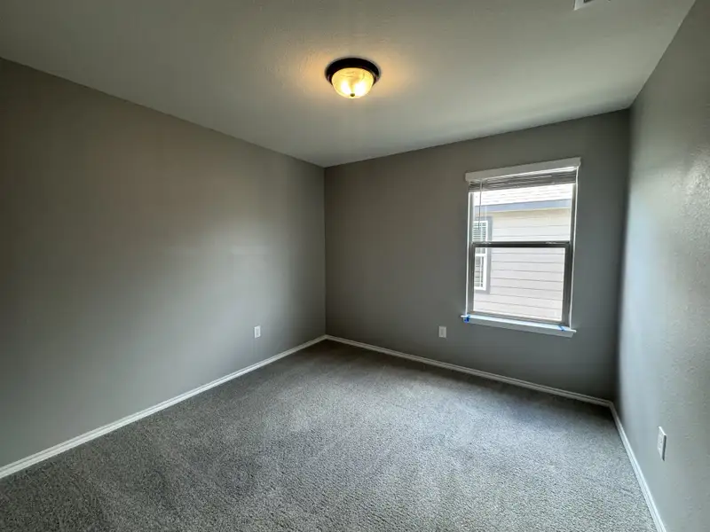A cozy bedroom featuring soft gray walls, plush carpeting, and a window with natural light.
