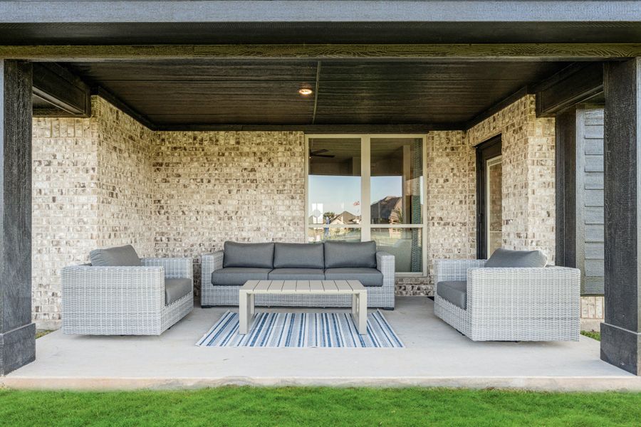 Covered patio with wicker sofa, two chairs, and coffee table on brick-walled outdoor living space