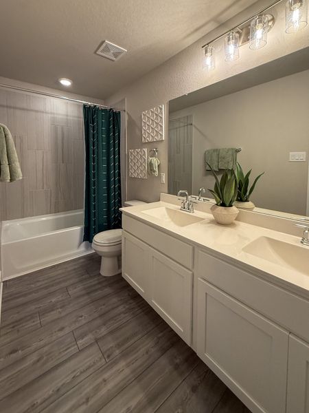 A modern bathroom with dual sinks, wood-style floors, and chic lighting over a sleek vanity.