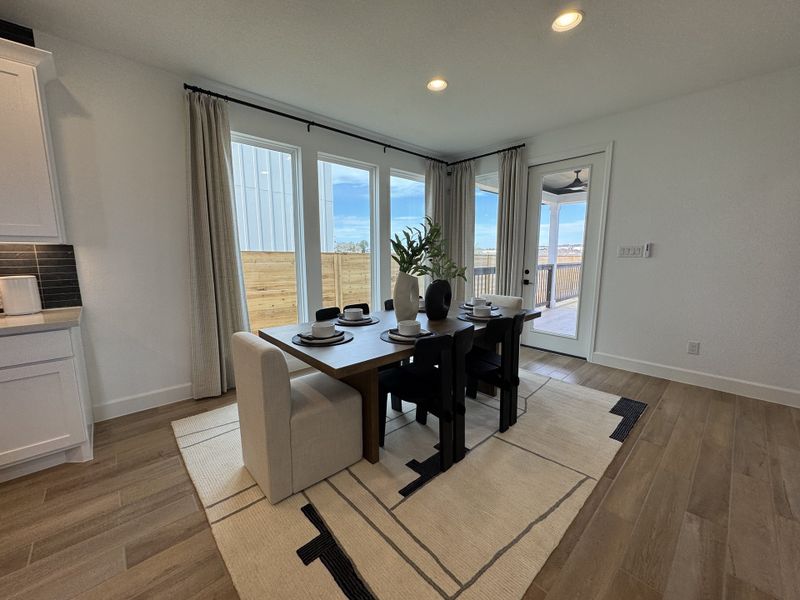 A bright dining area featuring a sleek wooden table, cozy seating, and large windows with a view of the patio.