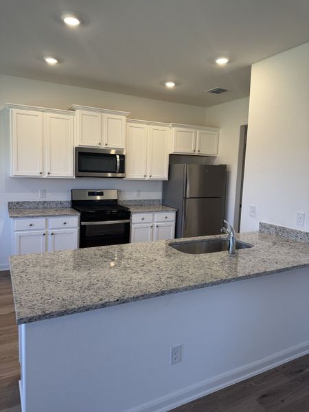 A modern kitchen with granite countertops, white cabinets, stainless steel appliances, and recessed lighting.