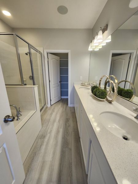 A modern bathroom featuring sleek quartz countertops, a spacious glass shower, and elegant wood flooring.